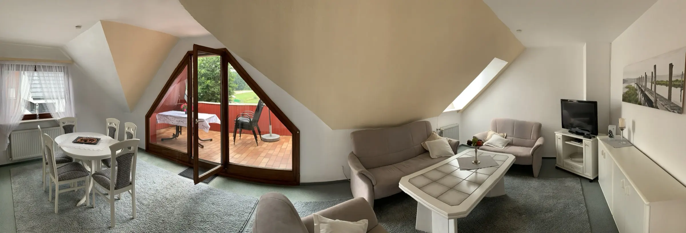Wohn- und Esszimmer der Ferienwohnung mit Sitzgruppe, Essplatz und offener Balkontür